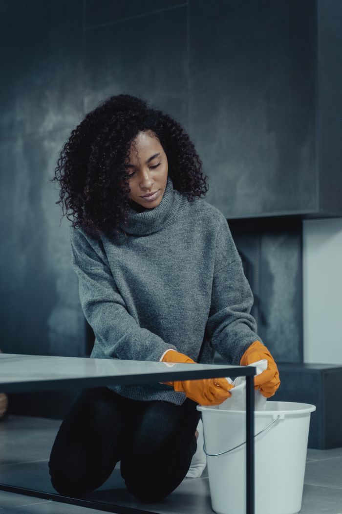 gallery-04 African American woman in gray sweater cleaning with a pail and gloves at home.